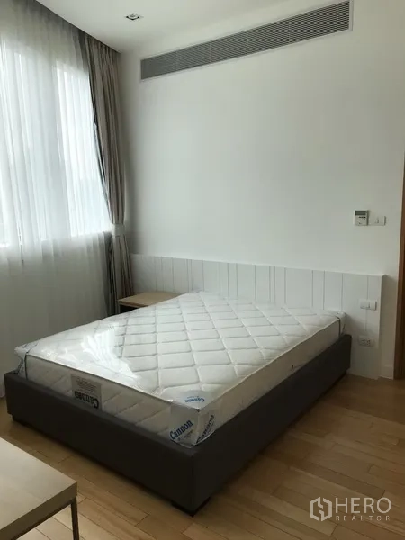 Condominium for rent in Khlong Toei, Bangkok - Light-filled secondary bedroom with large window, sheer curtains and bedside table.