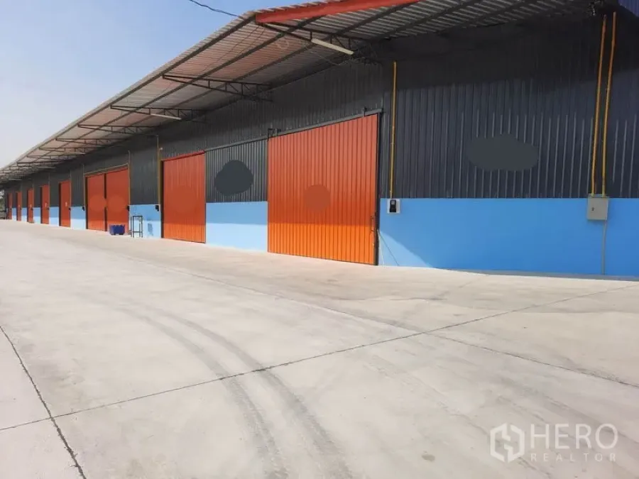 Warehouse for rent in Khlong Luang, Pathum Thani - Row of new warehouse units in Khlong Luang with orange sliding doors, covered loading bay and wide concrete driveway.