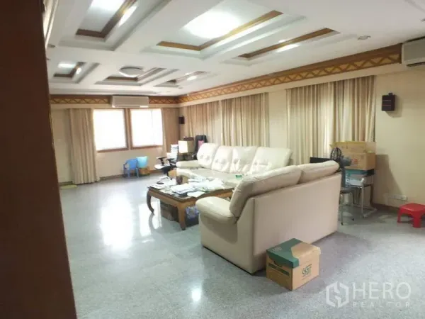 Detached House for rent in Bang Rak, Bangkok - Spacious living room with coffered ceiling, cream sectional sofa, large curtained windows and polished stone floors.