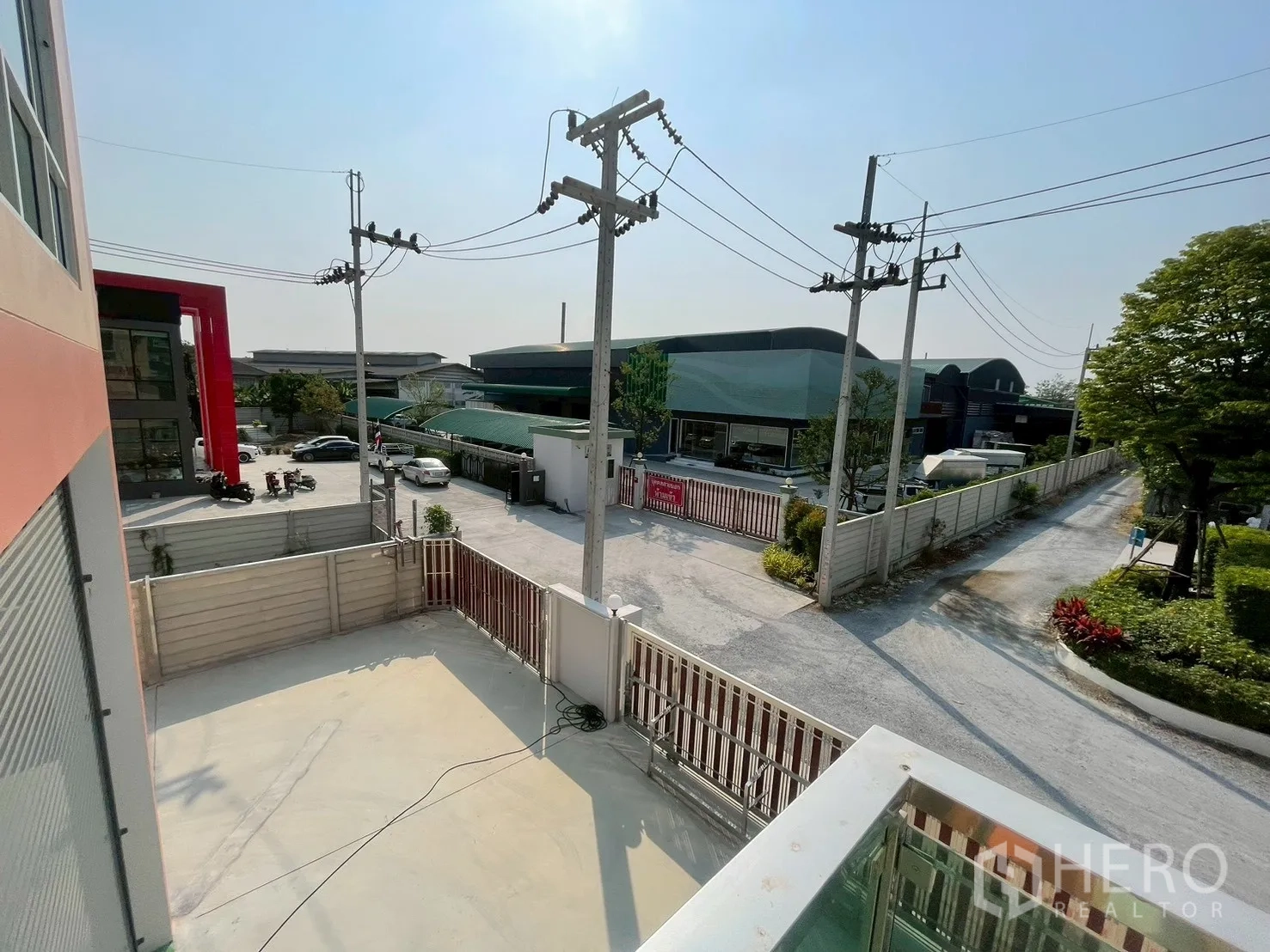 Factory for sale in Sam Phran, Nakhon Pathom - Upper-floor balcony looking over the concrete yard, front gate, and neighboring warehouses.