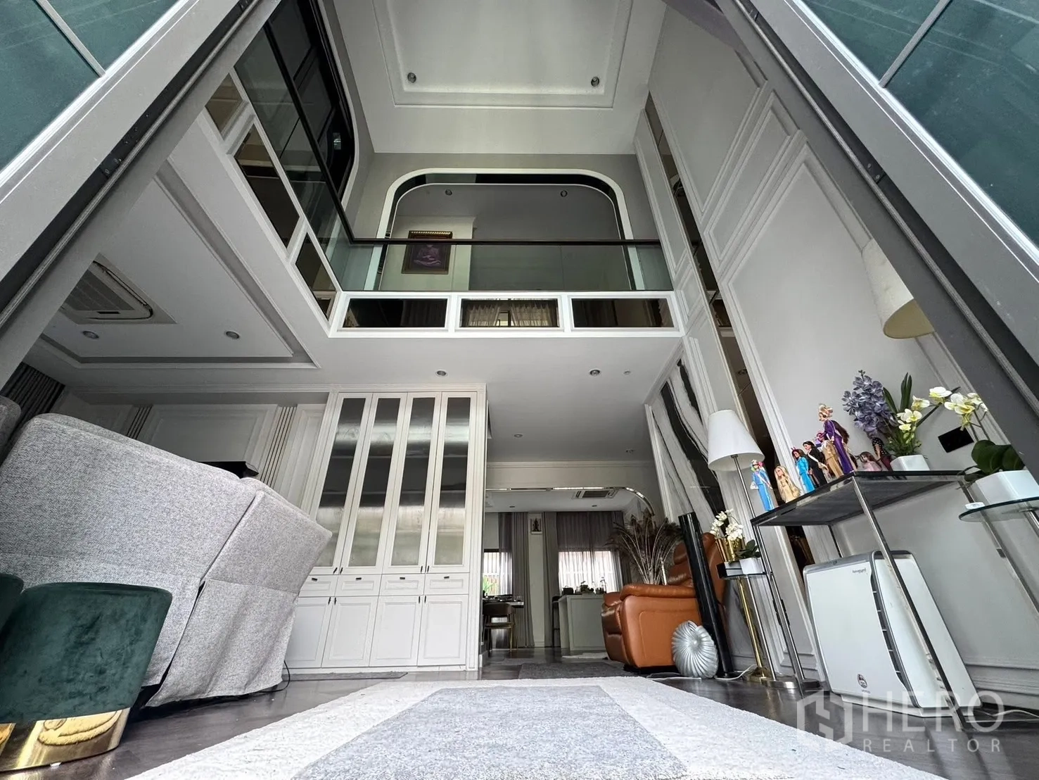 Detached House for sale in Mueang Pathum Thani, Pathum Thani - Double‑height living room with mezzanine glass balustrade and built‑in cabinets.