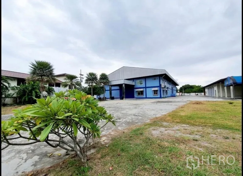 โรงงาน ขายในChon Buri - อาคารโรงงานสีน้ำเงิน สนามคอนกรีตกว้างและสนามหญ้า ใต้ท้องฟ้ามีเมฆ