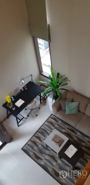 Condominium for rent in Khlong Toei, Bangkok - Cozy lounge with work desk, sofa and rug under tall windows and natural light.