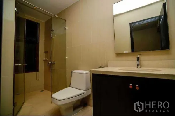 Condominium for rent or sale in Khlong Toei, Bangkok - Neutral-tone bathroom featuring a glass shower enclosure, vanity and toilet.