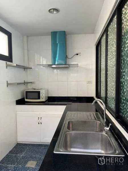 Townhouse for rent in Khlong Toei, Bangkok - Separate Thai kitchen with double sink, black countertop, hood, and sliding windows.