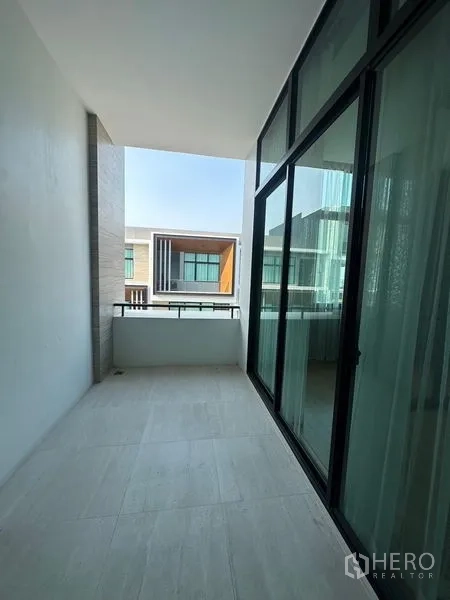 Townhouse for sale in Saphan Sung, Bangkok - Covered balcony with glass doors and railing overlooking neighboring modern townhouses.