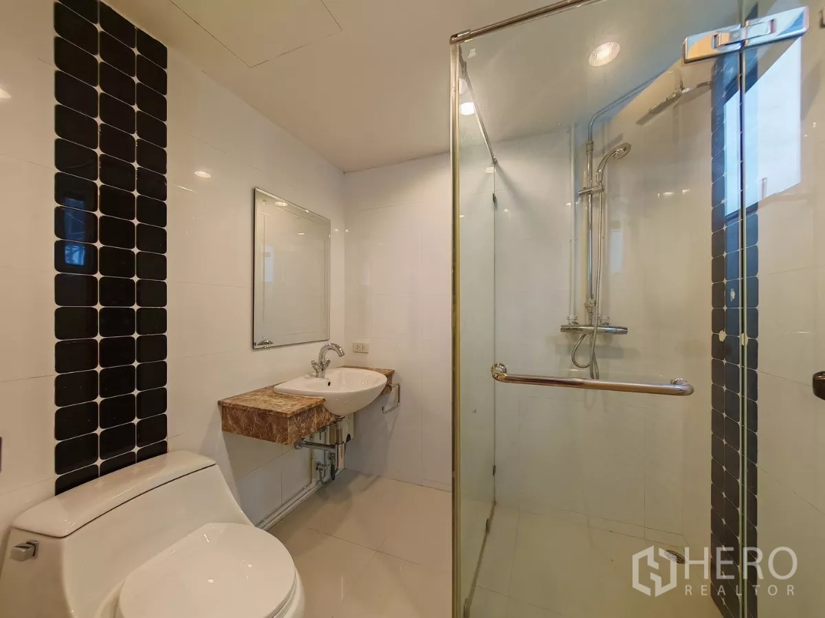 Condominium for rent in Pathum Wan, Bangkok - Bathroom with glass shower, toilet and vertical black tile accent.