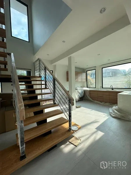 Detached House for rent in Watthana, Bangkok - Bright open-plan living area with floating wooden staircase and large windows beside a modern kitchen.
