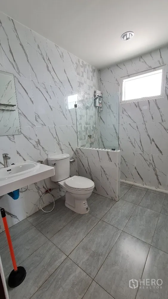 独栋房屋 for rent in Lat Phrao, Bangkok - 浴室铺大理石纹瓷砖，设马桶、台盆与玻璃隔断淋浴。