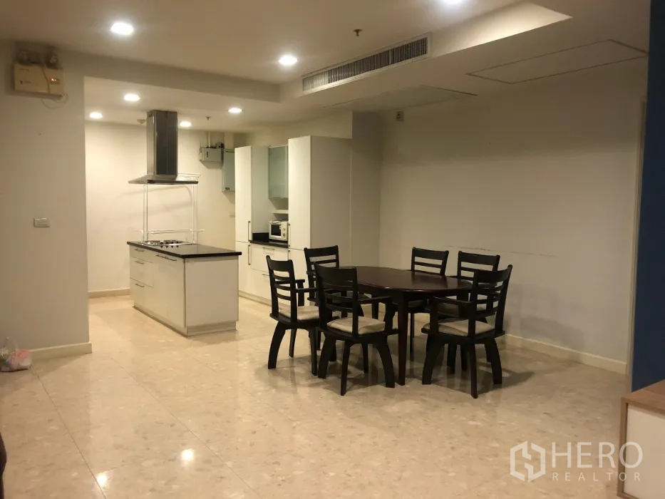 Condominium for sale in Khlong Toei, Bangkok - Dining area and open kitchen with a round table, recessed lighting and a central island.