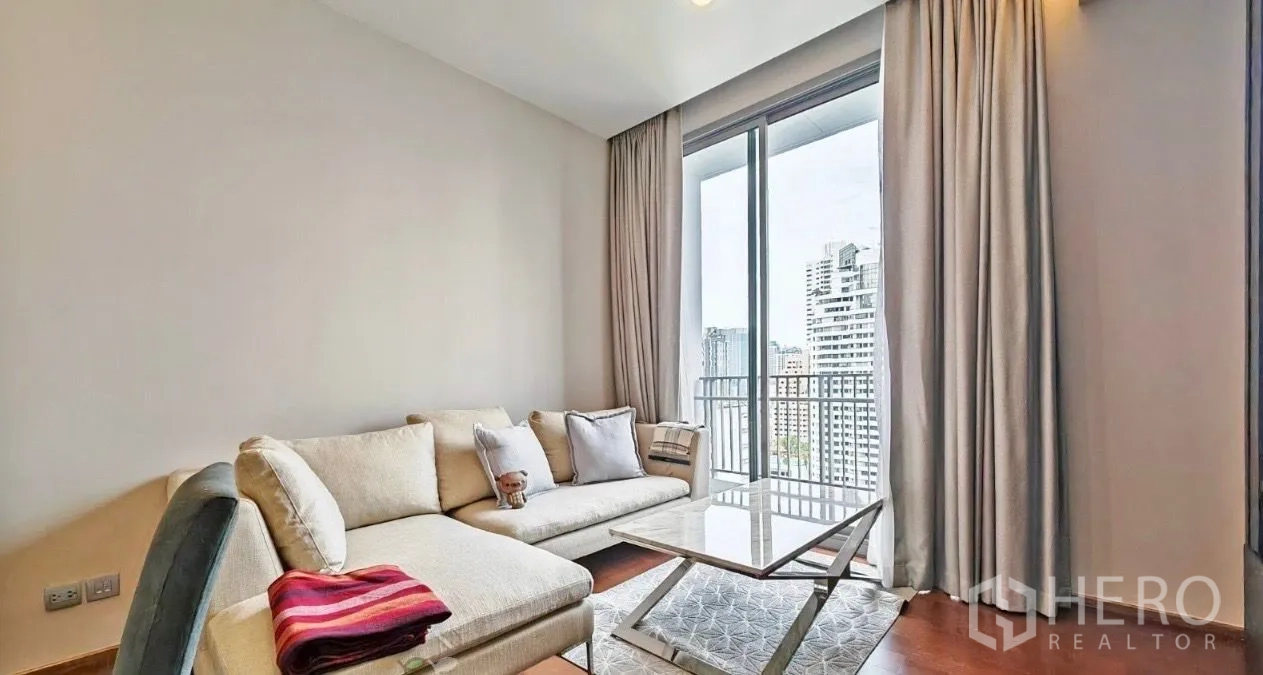 Condominium for rent in Watthana, Bangkok - Bright corner living area with a cream sectional sofa, marble coffee table, and floor-to-ceiling windows opening to a city-view balcony.