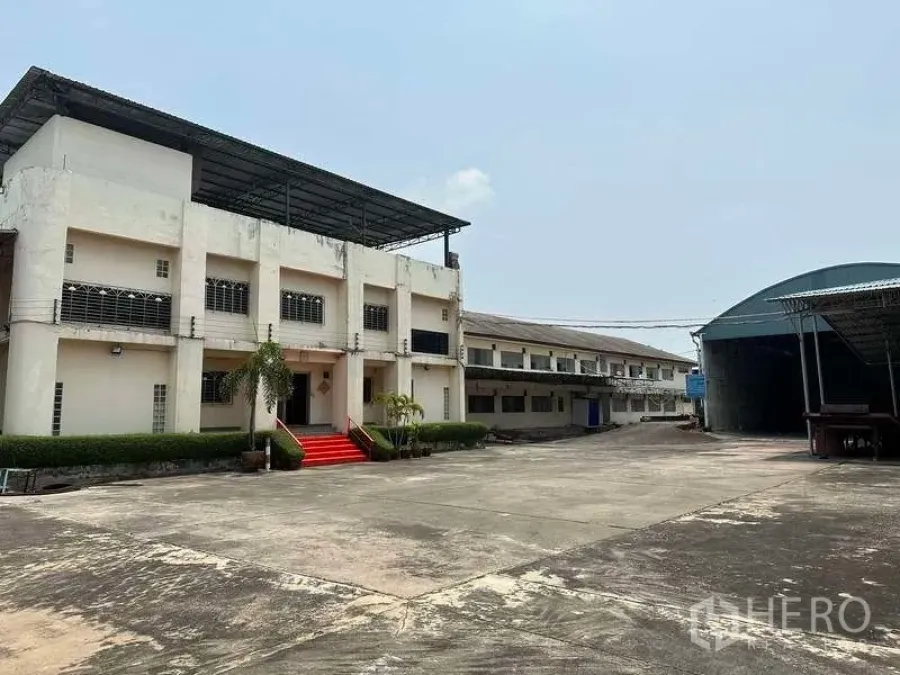 Factory for rent or sale in Bang Phli, Samut Prakan - Two-storey factory office with red steps facing a wide concrete yard and covered warehouse shed.