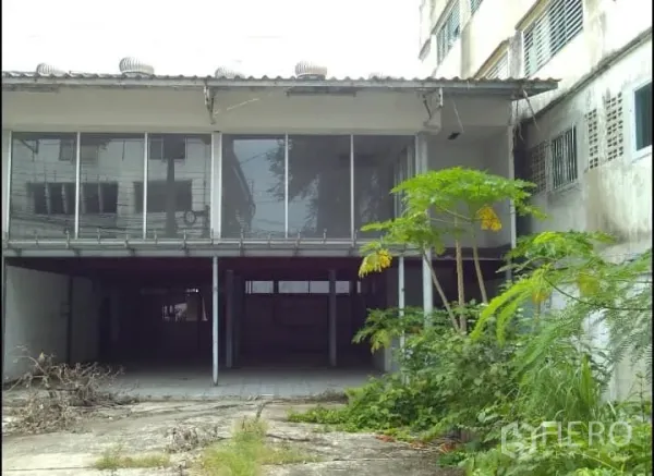 Warehouse for rent or sale in Bang Kho Laem, Bangkok - Side view of raised, glass-fronted warehouse with a covered loading bay and surrounding greenery.