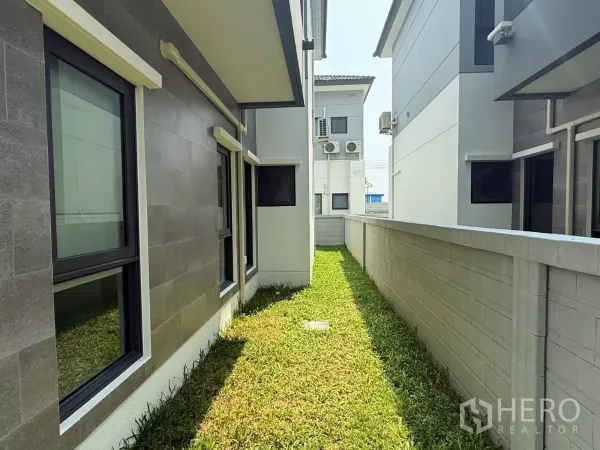 Detached House for rent in Bang Phli, Samut Prakan - Narrow side yard with grass between the house facade windows and boundary wall.