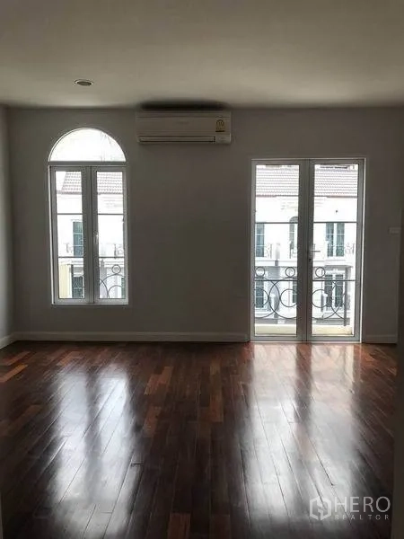 Townhouse for rent in Watthana, Bangkok - Bedroom with arched window and balcony doors overlooking the compound.