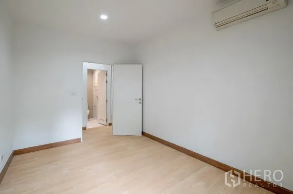 Condominium for sale - Empty air-conditioned bedroom with wood flooring and doorway to an en-suite bathroom.