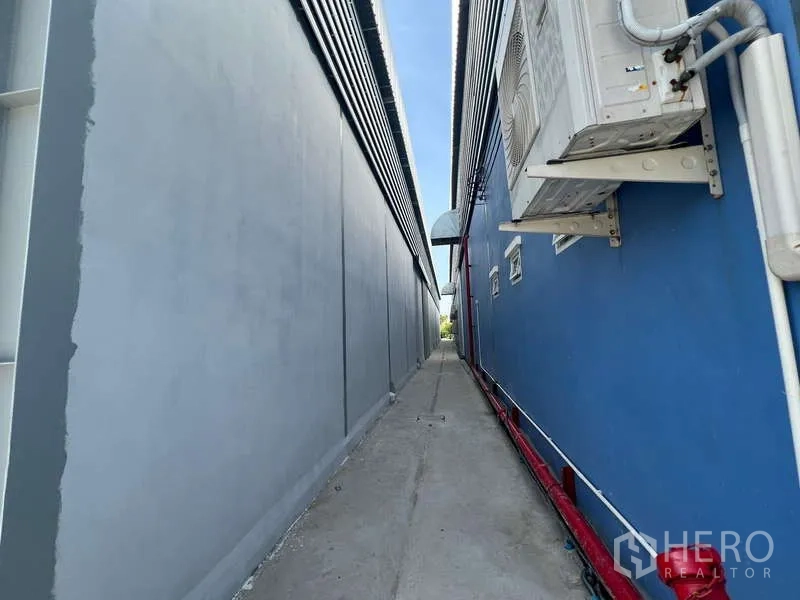 Warehouse for rent in Prawet, Bangkok - Narrow service walkway along the warehouse side wall with external piping and AC units.