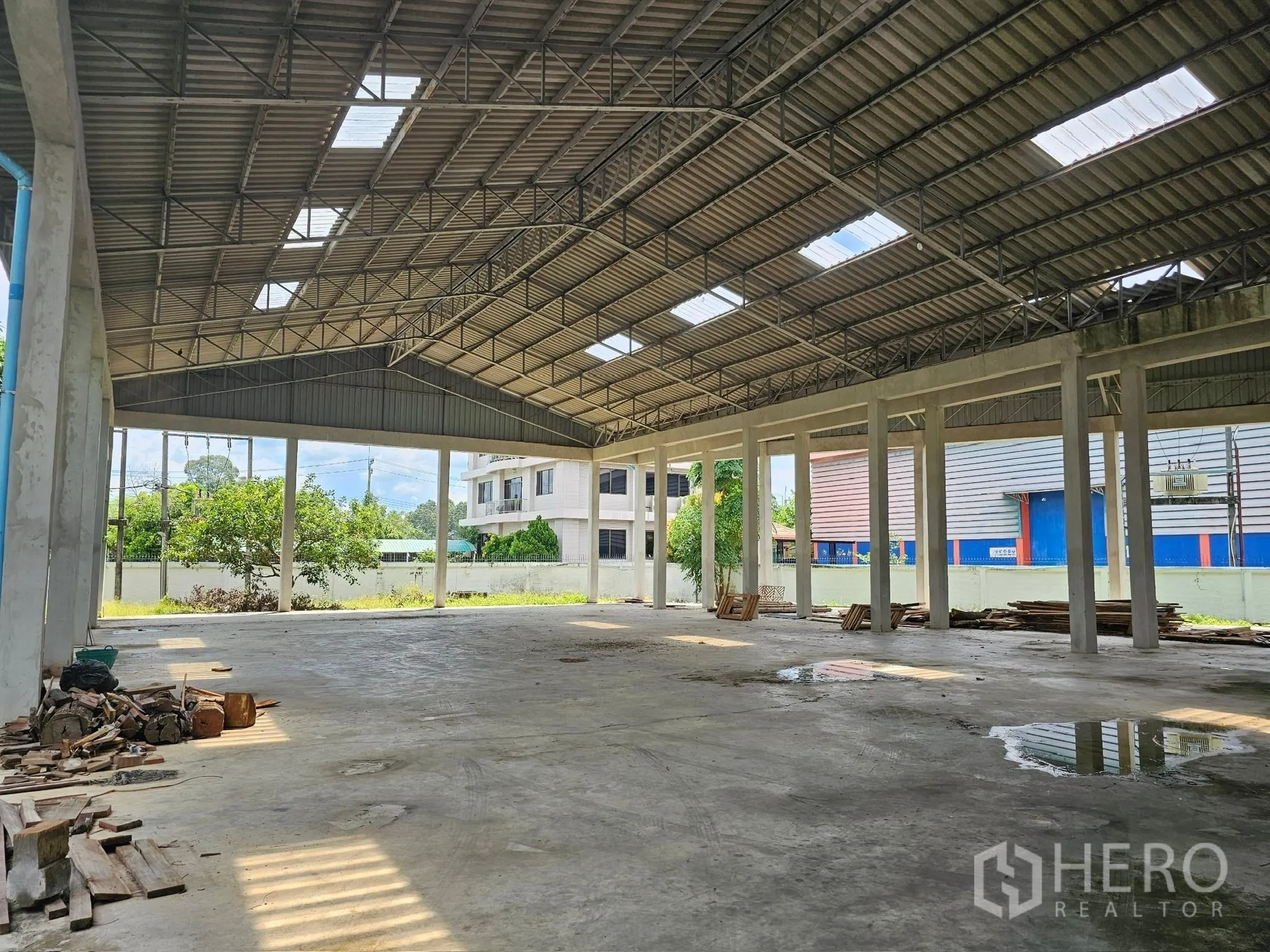 Factory for rent or sale in Mueang Rayong, Rayong - Open-sided warehouse bay with tall columns, metal roofing and views of the yard with trees and nearby buildings.