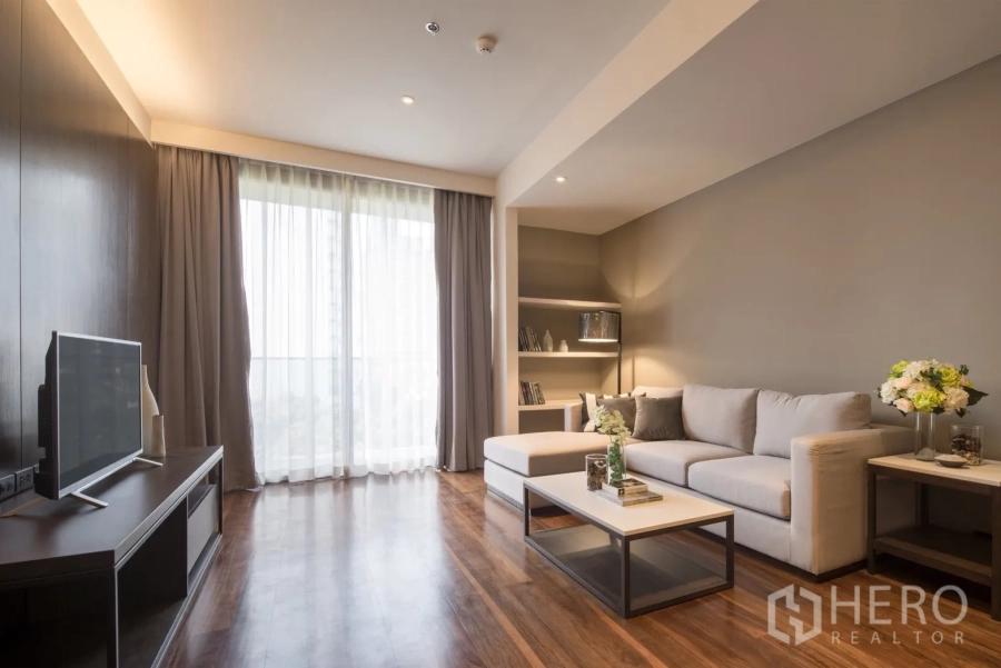 Condominium for rent in Khlong Toei, Bangkok - Bright living room with L-shaped sofa, coffee table and floor-to-ceiling window in a 2-bedroom condo near BTS Phrom Phong.