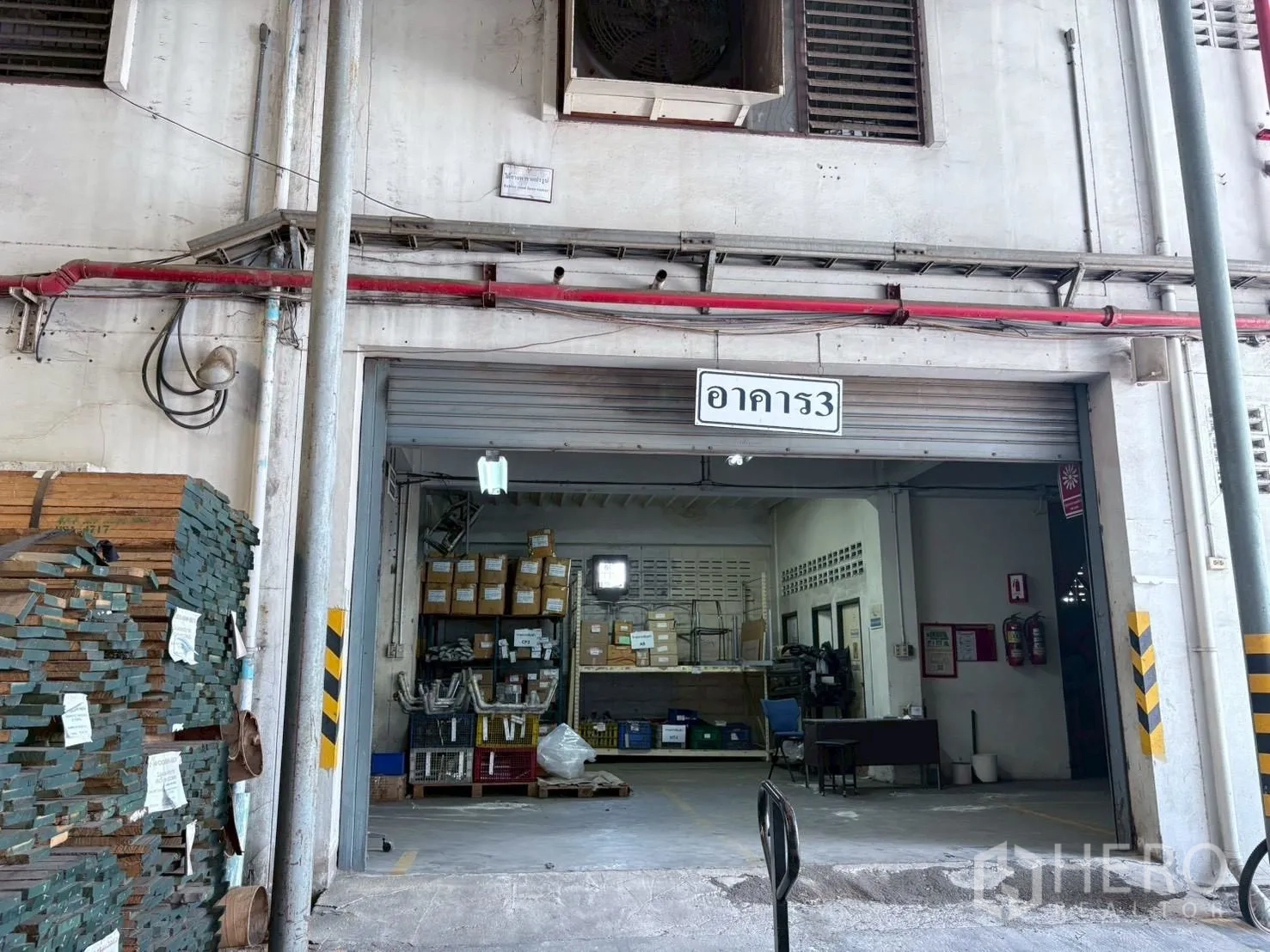 Factory for rent or sale in Bang Khun Thian, Bangkok - Entrance to a warehouse room with shelving, materials and a half-open roller door.