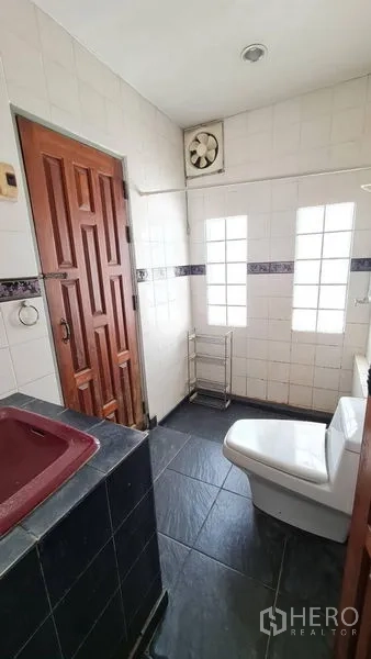 Detached House for rent in Lat Phrao, Bangkok - Tiled bathroom with glass-block windows, ventilation fan and wooden door.