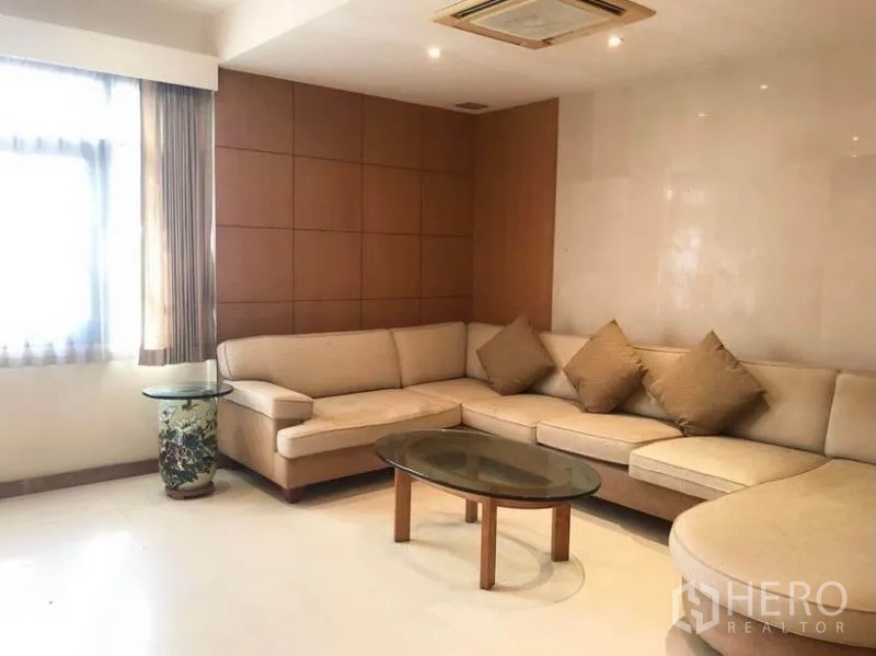 Detached House for sale in Mueang Samut Prakan, Samut Prakan - Cozy family lounge with L-shaped sofa, wood panel wall and glass coffee table.