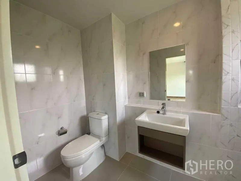 Detached House for rent in Khan Na Yao, Bangkok - Clean tiled bathroom with toilet, vanity sink and wall mirror.