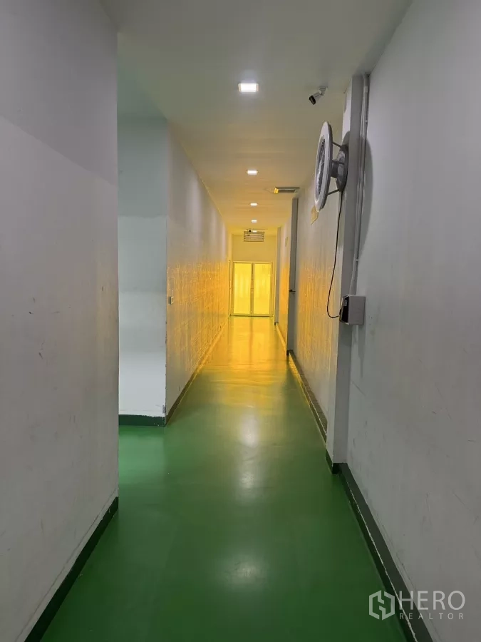 Factory for sale in Lam Luk Ka, Pathum Thani - Long hallway with epoxy flooring, wall fan and a brightly lit clean area at the end.