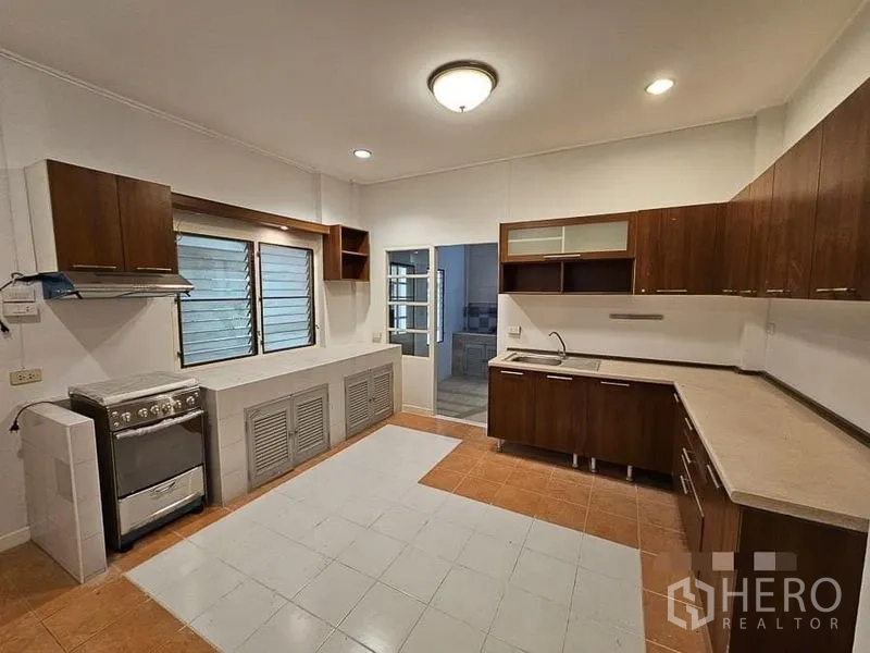 Detached House for rent - Separate Thai kitchen featuring U-shaped wooden cabinets, stove, and ample worktop space.
