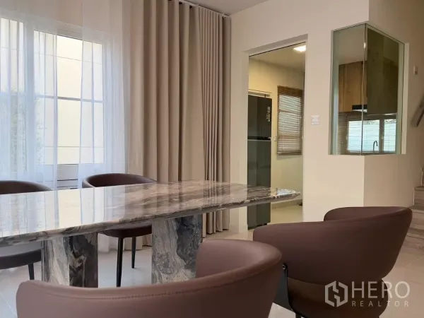 Detached House for rent in Bang Phli, Samut Prakan - Close-up of dining zone with marble table, upholstered chairs and doorway to the kitchen.