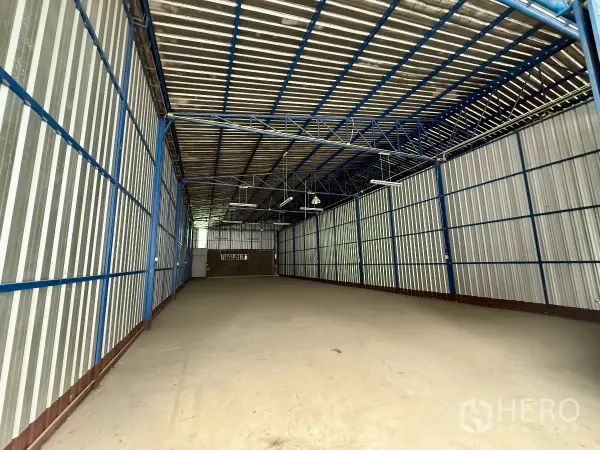 Warehouse for rent in Bueng Kum, Bangkok - Wide-angle view of 290 sqm warehouse showing clear span, corrugated metal walls and hanging lights.