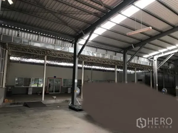 Warehouse for rent in Pak Kret, Nonthaburi - Spacious warehouse interior with high steel roof, skylights, concrete floor and glass-partitioned office area.