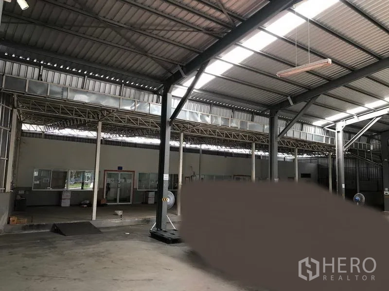 Warehouse for rent in Pak Kret, Nonthaburi - Spacious warehouse interior with high steel roof, skylights, concrete floor and glass-partitioned office area.