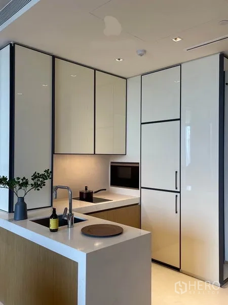 Condominium for rent in Khlong Toei, Bangkok - Compact L-shaped kitchen with glossy cabinetry, built-in appliances and quartz countertops.