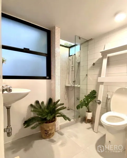 Townhouse for rent in Khlong Toei, Bangkok - Contemporary bathroom with glass shower enclosure, white tiles and potted plants.