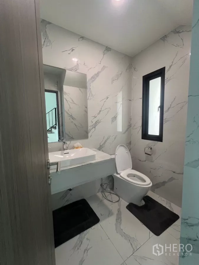 Detached House for rent in Lat Phrao, Bangkok - Modern guest bathroom with marble-pattern tiles, window, white basin and toilet.