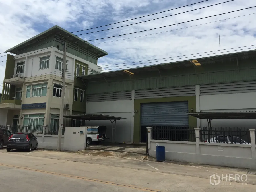 Factory for sale in Pathum Thani - Modern factory with attached three-storey office, wide roller shutter, covered loading bays and gated parking on a concrete road in Lam Luk Ka, Pathum Thani.