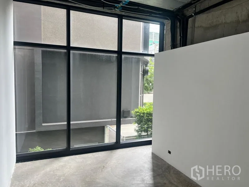 Retail Space for rent in Watthana, Bangkok - Compact room with large black-framed window and concrete floor for office or storage.