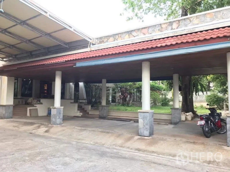 Detached House for rent in Bang Phli, Samut Prakan - Large covered carport with tiled roof, columns and driveway beside a small lawn.