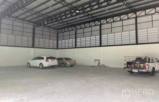 Warehouse for rent in Prawet, Bangkok - Spacious warehouse interior with high steel truss roof and open concrete floor, suitable for vehicle parking and storage.