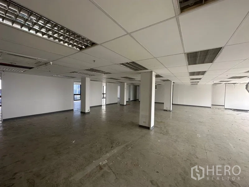 Office Space for rent in Khlong Toei, Bangkok - Spacious empty office zone with dropped ceiling, lighting panels and structural columns.