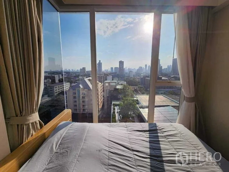 Condominium for rent in Khlong Toei, Bangkok - City skyline view from bedside through large glass windows with morning sun.