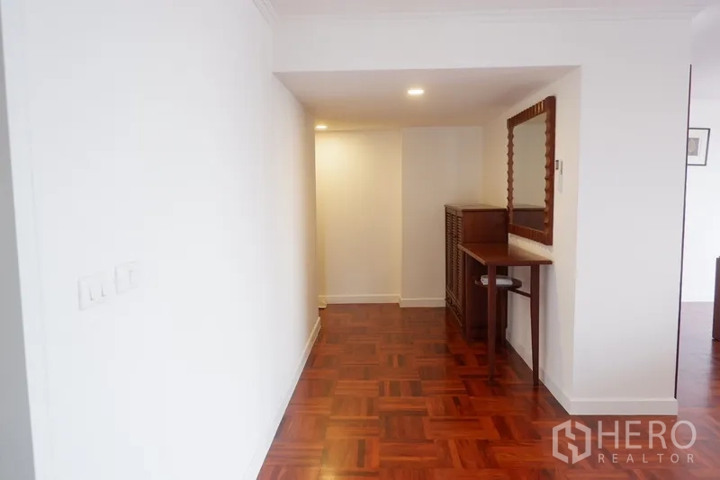 Condominium for rent in Khlong Toei, Bangkok - Hallway with polished wood floor, console table and large framed mirror under recessed lights.