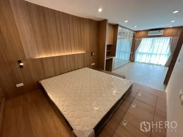 Home Office for rent in Khlong Toei, Bangkok - Spacious master bedroom with wood panel feature wall, platform bed and floor-to-ceiling windows.
