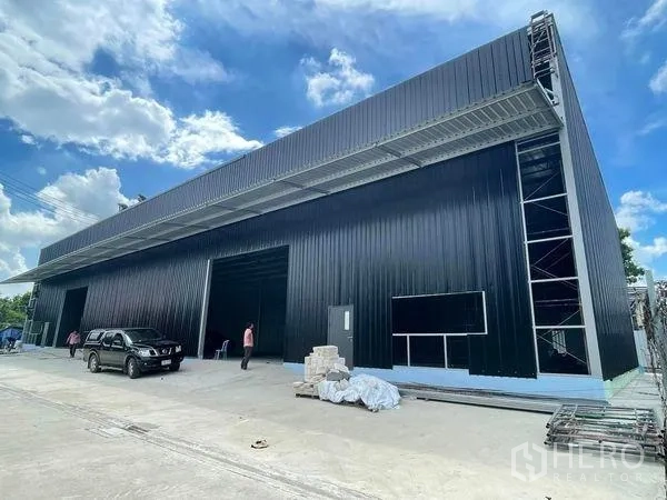 Warehouse for rent in Pak Kret, Nonthaburi - Modern black metal warehouse exterior with tall canopy and wide loading bays in Pak Kret, Nonthaburi.