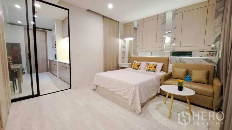 Condominium for sale in Pathum Wan, Bangkok - Open-plan bedroom and living area with bed, sofa, round coffee table and sliding glass door.