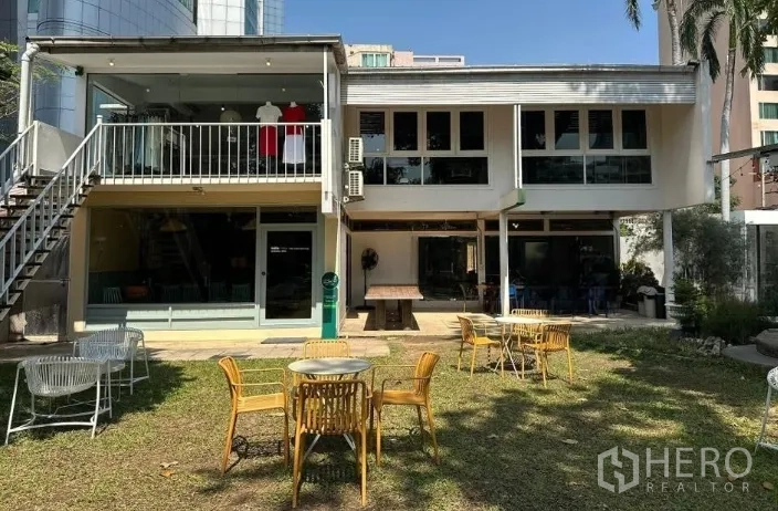 Retail Space for rent in Khlong Toei, Bangkok - Two-storey retail building with glass fronts, balcony, and a lawn with outdoor tables and chairs.