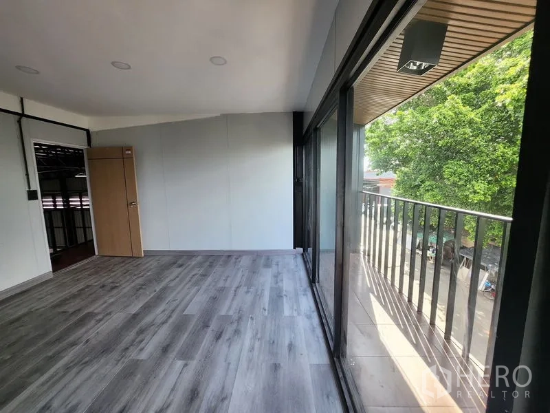 Warehouse for rent in Lam Luk Ka, Pathum Thani - Corner office with floor-to-ceiling windows and balcony railing facing trees.