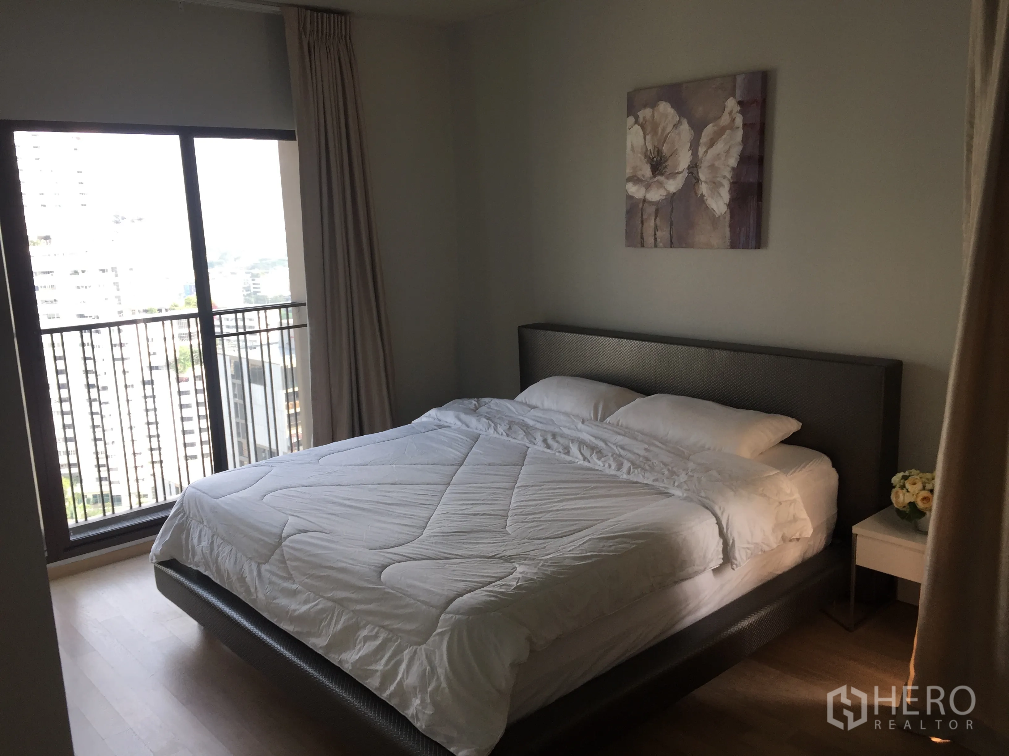Condominium for rent in Bangkok - Master bedroom with large bed, wall art, and sliding door to a balcony overlooking the city.