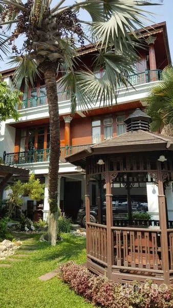 Townhouse for rent in Khlong Toei, Bangkok - Sunlit garden showcasing gazebo, palm trees and three-storey home.